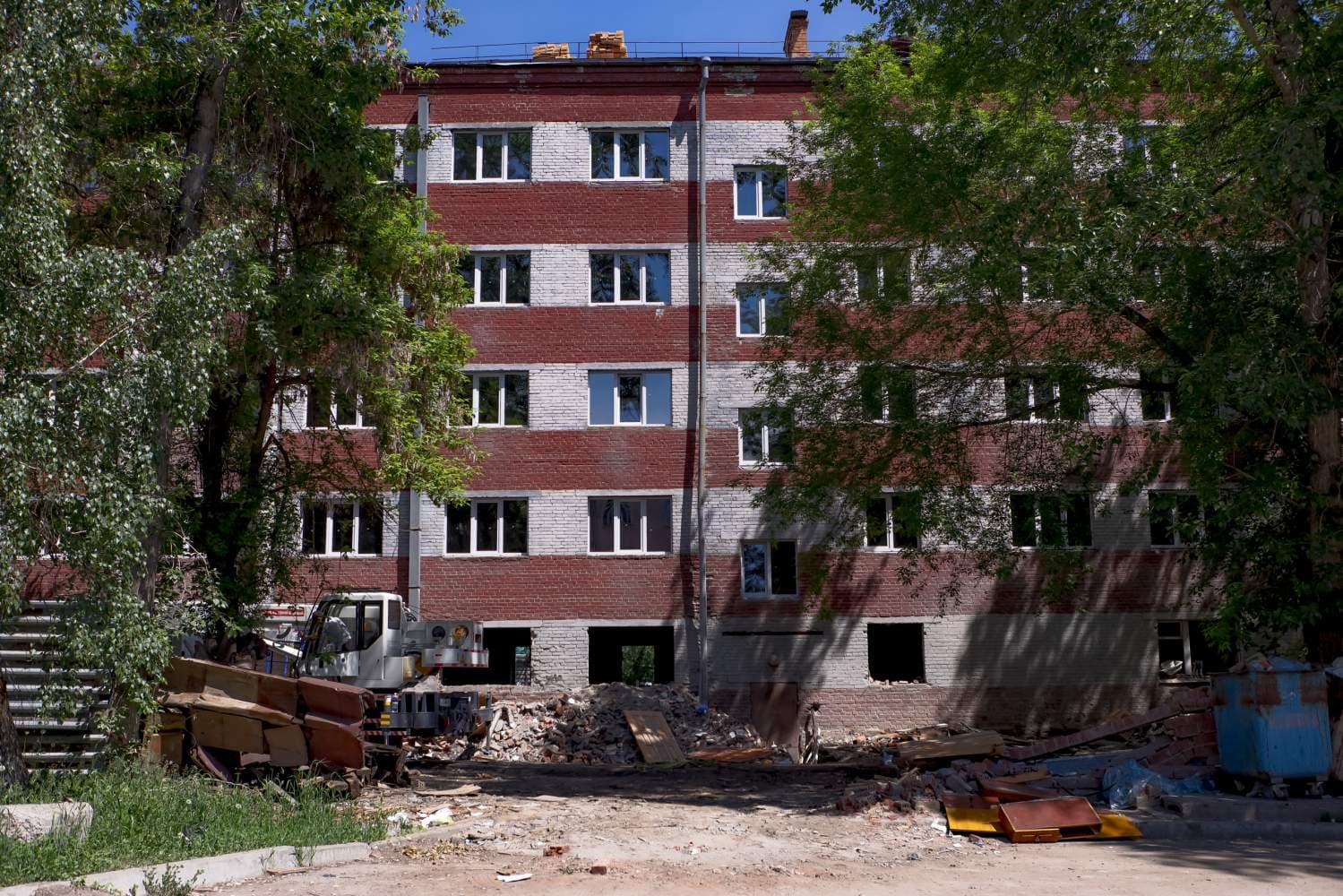 Общежитие №5 ИРНИТУ на Игошина, 2 во время капитального ремонта — пятиэтажный корпус из красного кирпича с белыми поясами, на первом этаже выбиты оконные и дверные проёмы, под стеной строительный мусор и автокран