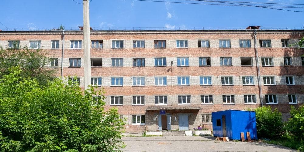 Общежитие №8 ИРНИТУ на Курчатова, 14 — пятиэтажный корпус из светлого силикатного кирпича с розовыми поясами и старыми деревянными рамами, у центрального входа синий строительный вагончик