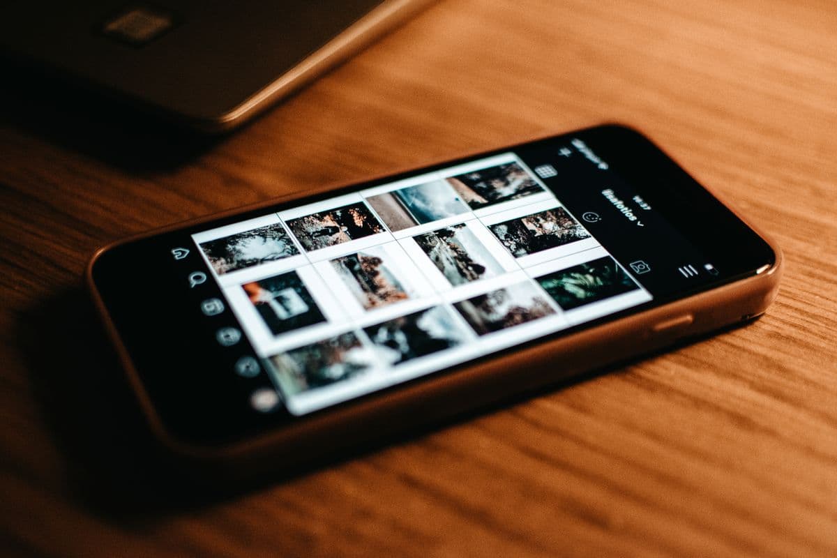 Смартфон с сеткой фотографий в галерее на деревянном столе рядом с ноутбуком