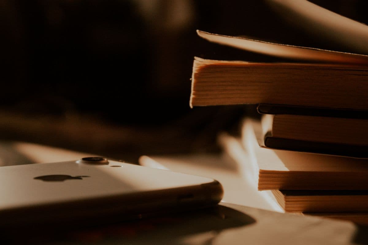 Стопка бумажных книг и белый смартфон в тёплом свете