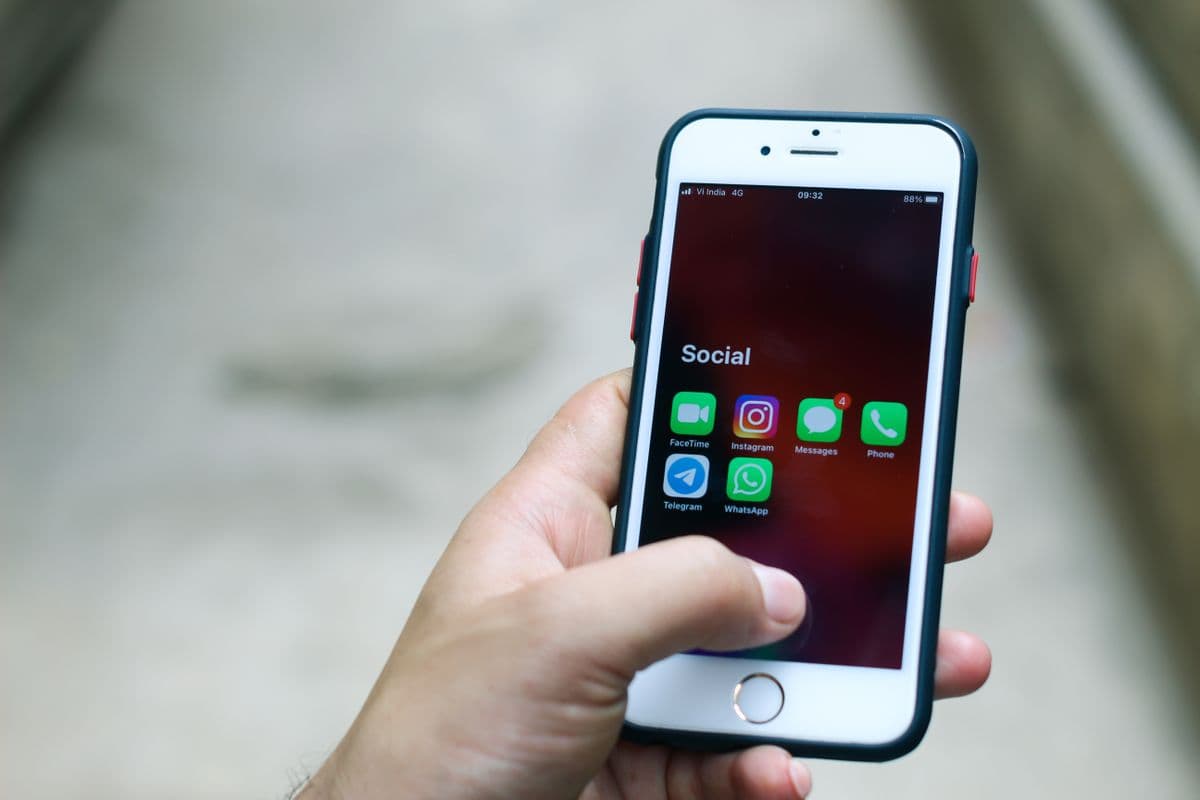 Рука держит iPhone с открытой папкой мессенджеров на экране, среди них Telegram