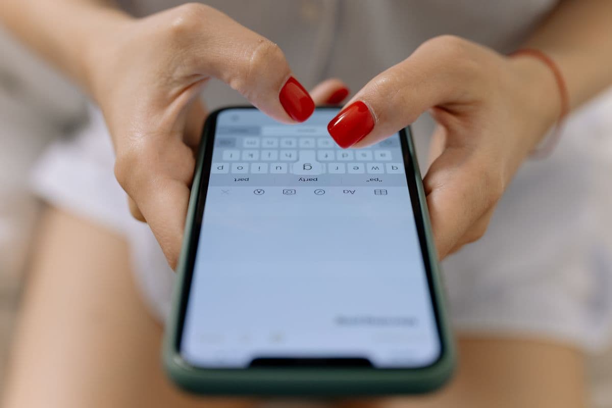 Женские руки с красным маникюром набирают сообщение на смартфоне в зелёном чехле