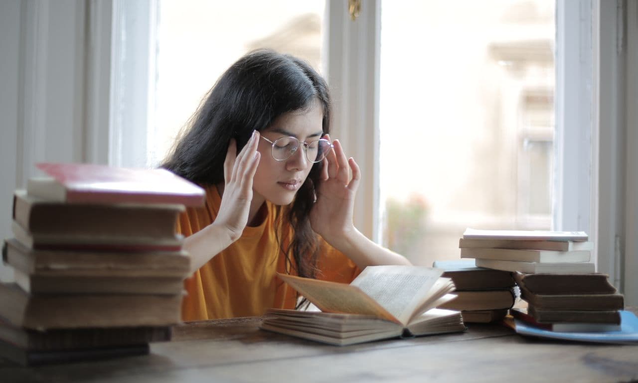 Уставшая студентка за столом с книгами после бессонной ночи