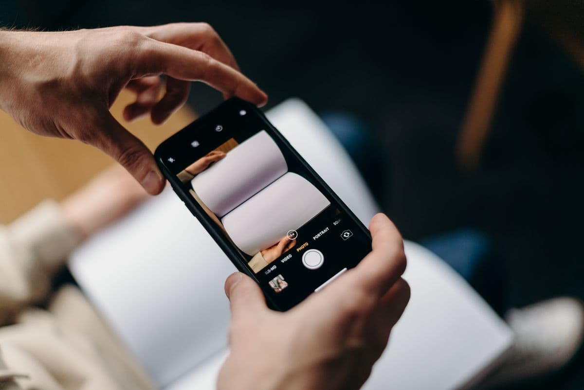 Руки держат смартфон в режиме камеры и фотографируют раскрытую тетрадь