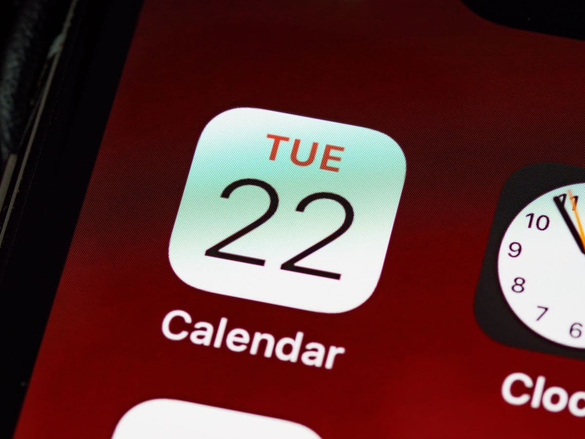 Экран iPhone крупным планом с иконкой приложения «Календарь» на тёмно-красном фоне