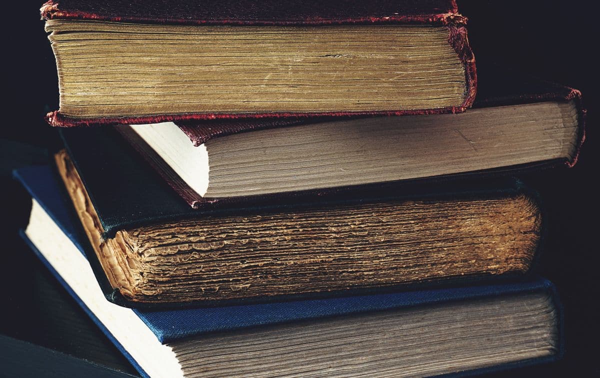 Школьница читает толстый роман за столом со стопкой книг