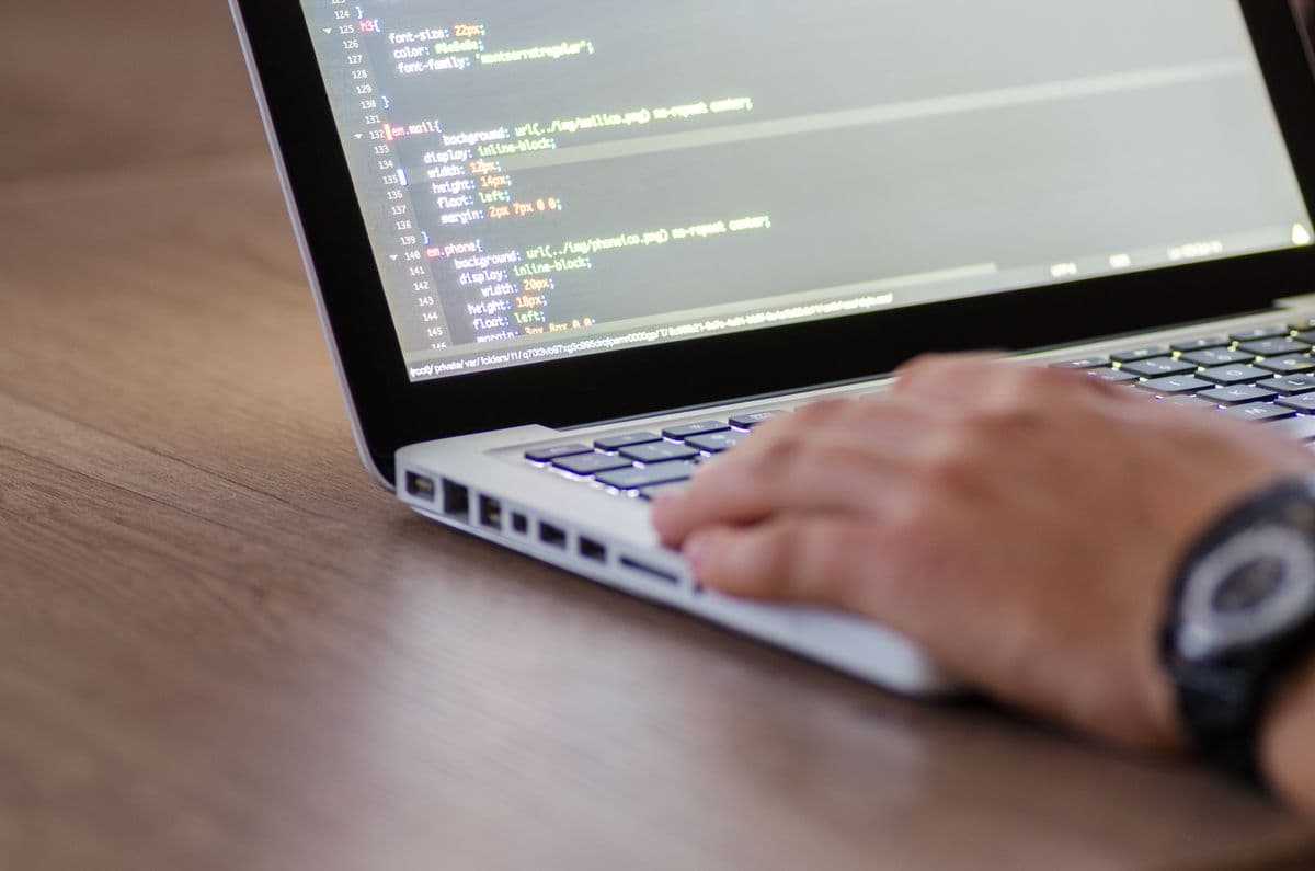 Рука печатает на серебристом ноутбуке, на экране код CSS с номерами строк