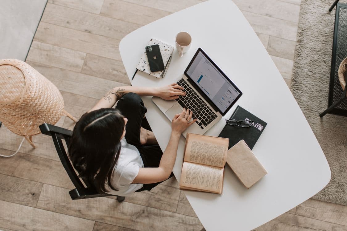 Студентка печатает конспект на ноутбуке, рядом открытая книга и блокнот