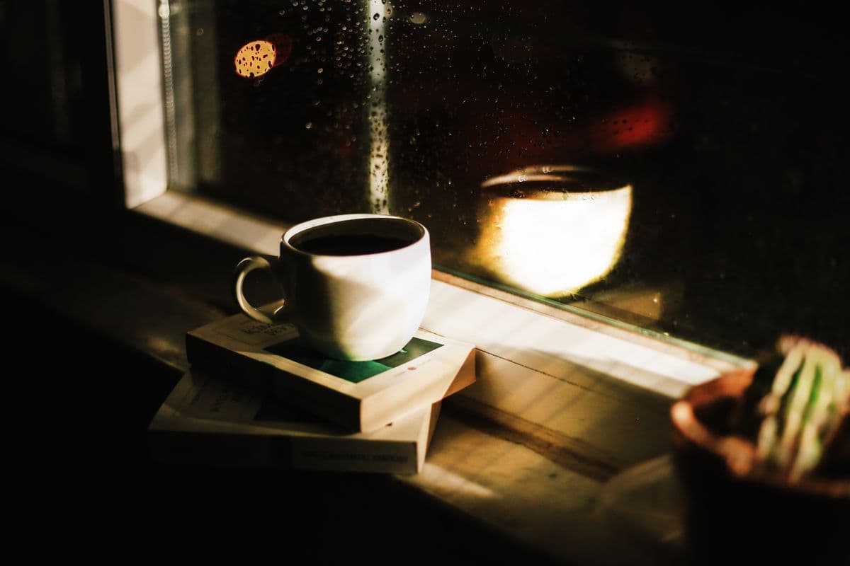 Чашка чёрного кофе на стопке книг у окна с каплями дождя пасмурным осенним вечером