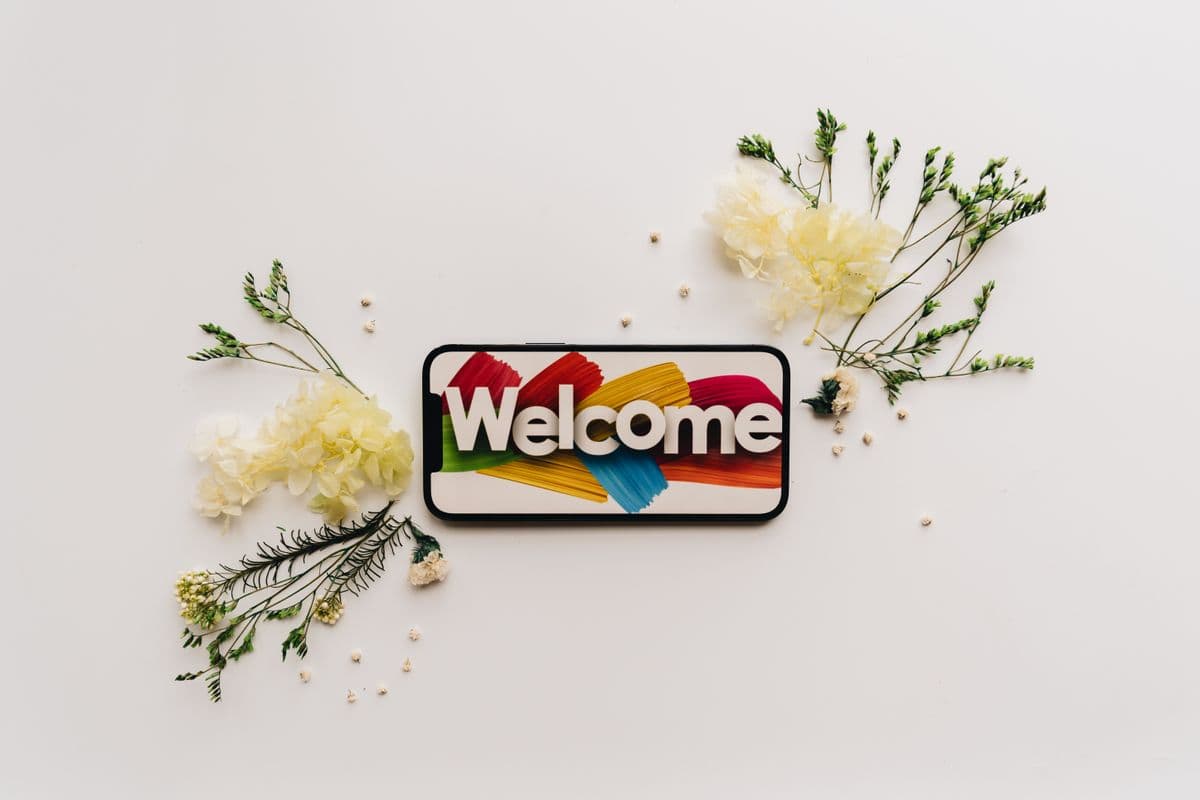 Смартфон с надписью Welcome на экране среди сухоцветов и веточек на белом столе