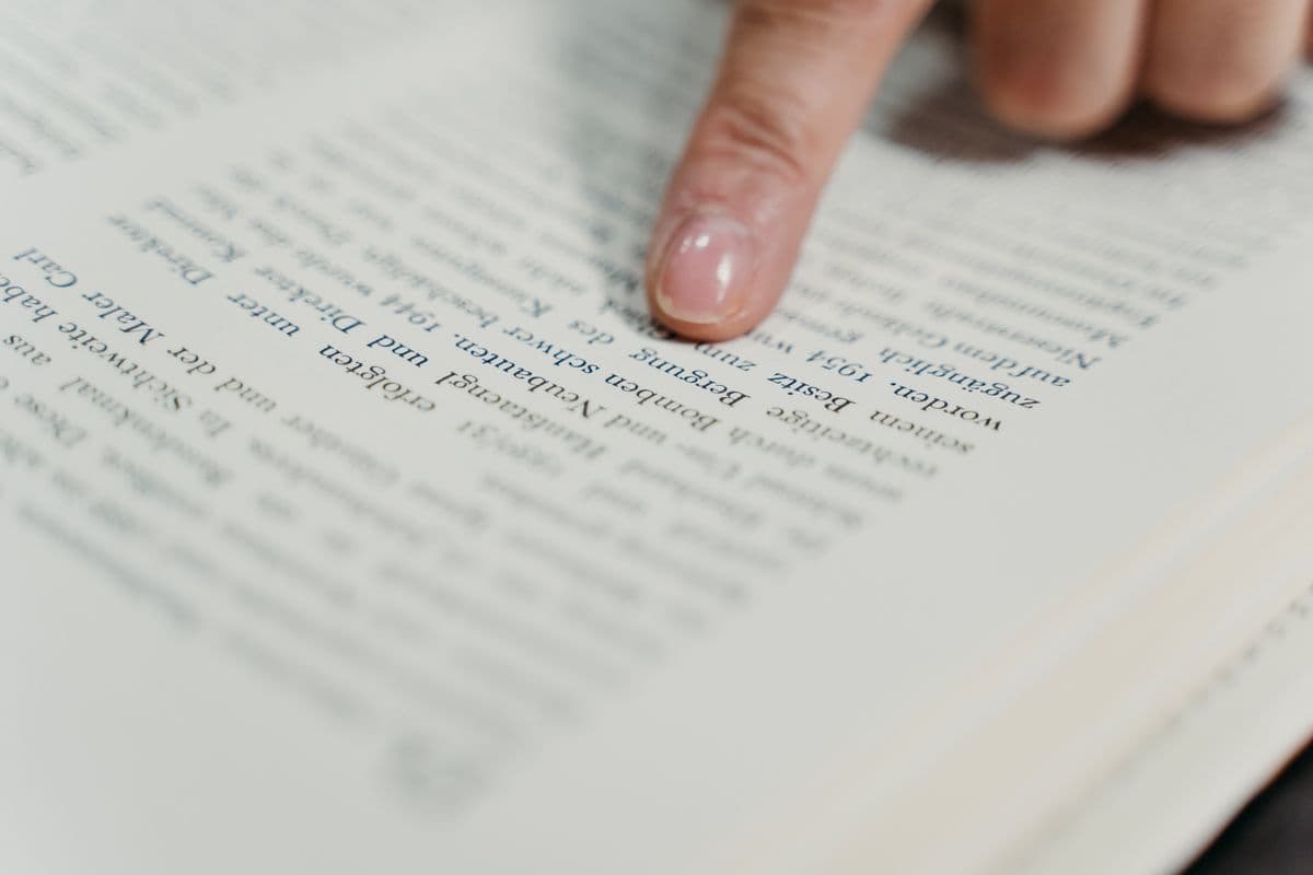 Палец ведёт по строке в открытой книге — приём чтения с указкой, остальной текст страницы размыт